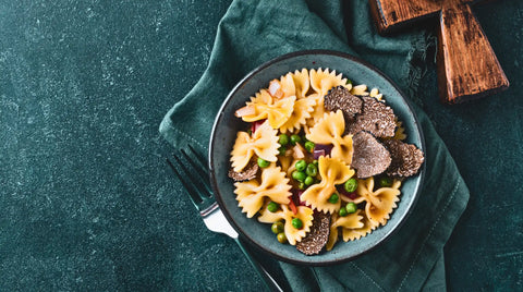 Un tazón de pasta farfalle con guisantes y trufas negras en rodajas