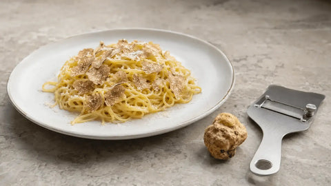Fresh Tuber borchii shaved over tagliolini, with a whole truffle and truffle slicer beside the plate
