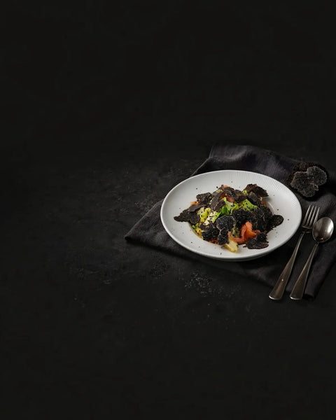 Salmon salad topped with fresh black truffle shavings beside a cut truffle