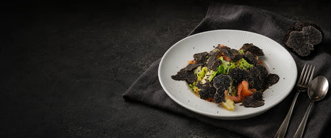 Salmon salad topped with fresh black truffle shavings beside a cut truffle